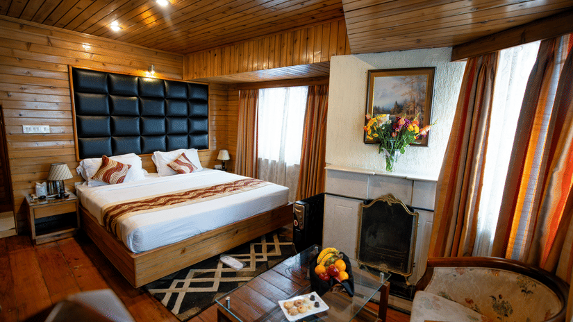 A cosy attic duplex bedroom at Viceroy Hotel, Darjeeling, featuring warm wooden interiors, fireplace, plush bed, and inviting seating for a charming mountain retreat.