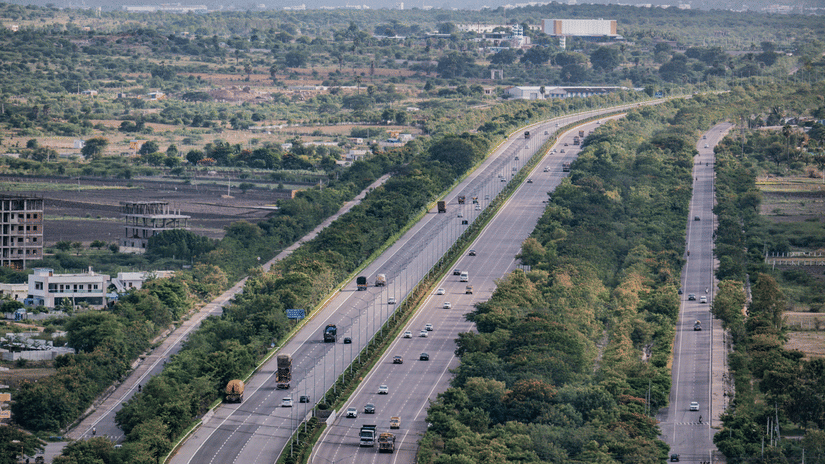 An aerial view shows a multi-lane highway surrounded by greenery and urban landscape.