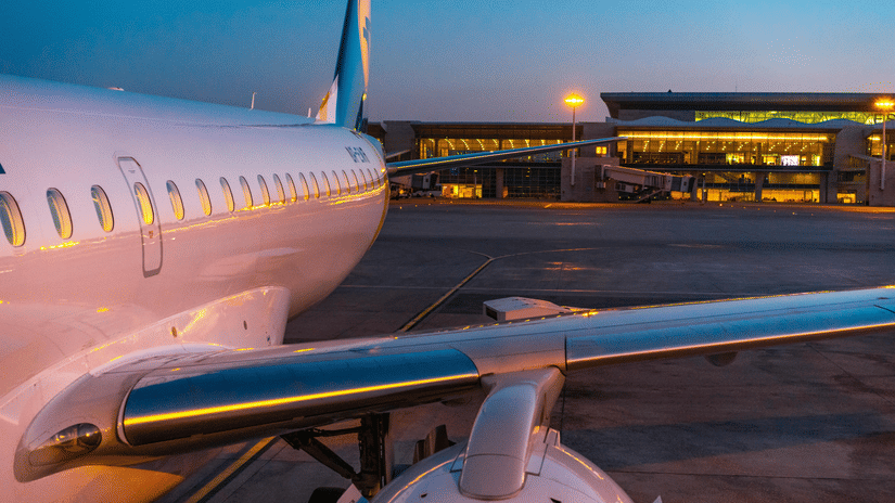 A passenger airplane parked at an airport runway during evening with terminal lights in the background.