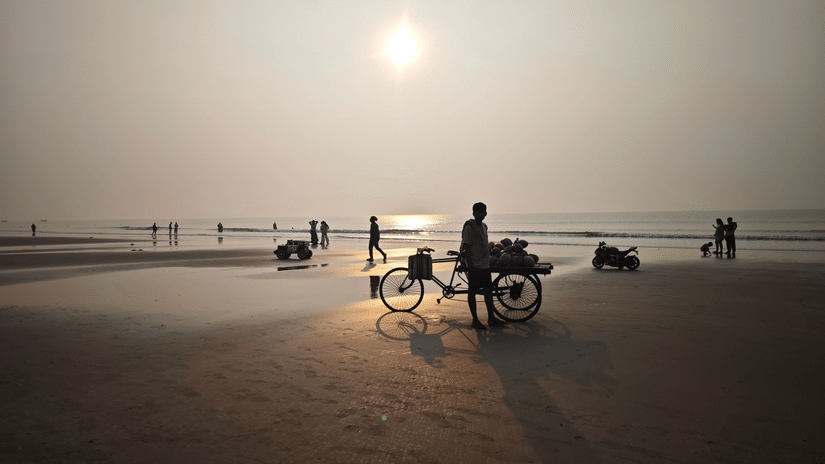 Silhouetted visitors and a vendor cart on a beach during sunrise.