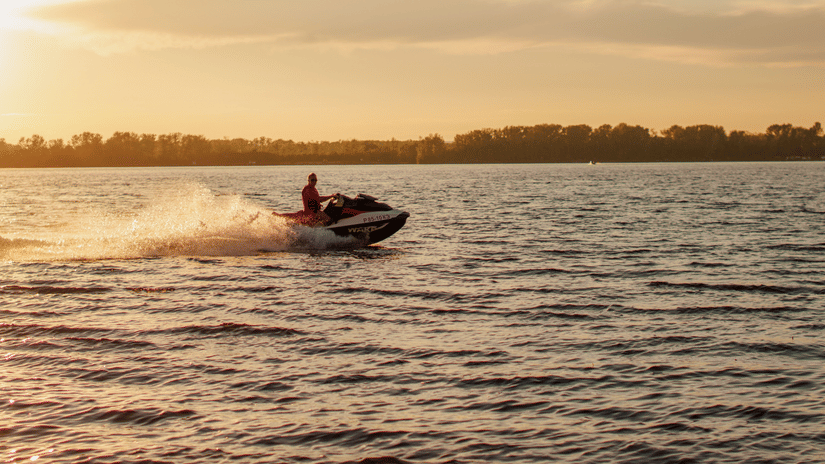 Person riding a jet ski across calm waters during a golden sunset.