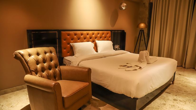 A king bed with a plush headboard and a single seater sofa next to the bed inside one of the rooms at VITS Nanded Hotel.
