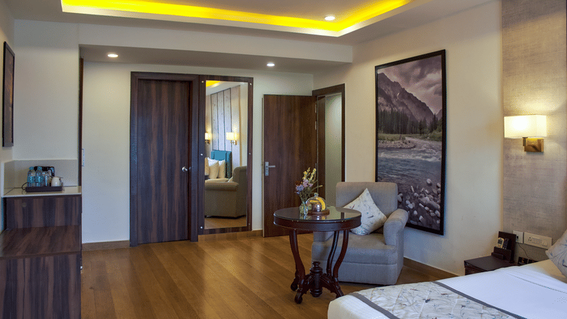 A corner view of the Suite with bed, wooden flooring, open doorway to adjoining space, and recessed ceiling lights at Voyage Milestone Hotel and Banquet.