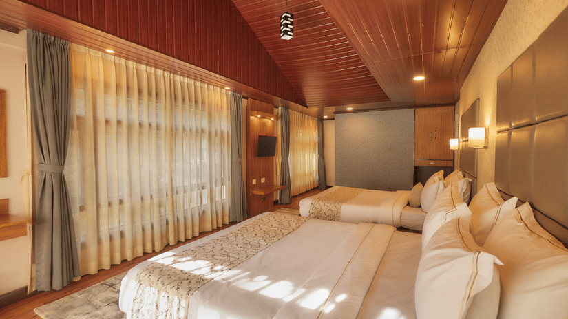 A spacious double bedroom with twin beds, dark wood flooring, and soft warm lighting from wall sconces | Voyage Rodhi Resort