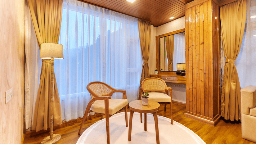 A seating area with two wooden chairs, a round table, and a floor lamp by the window | Voyage Rodhi Resort