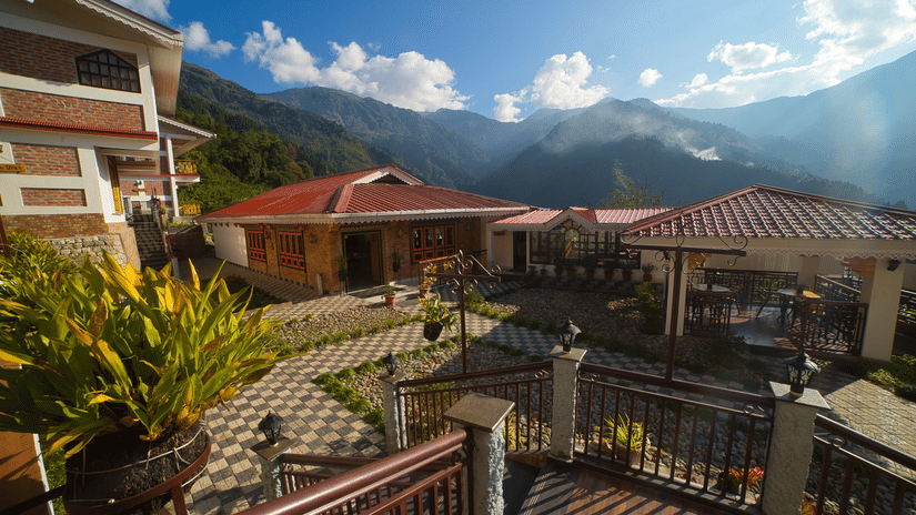 Exterior view of the hotel courtyard with red-roofed buildings, tropical plants, and a breathtaking mountain backdrop at Voyage Songfum Retreat.