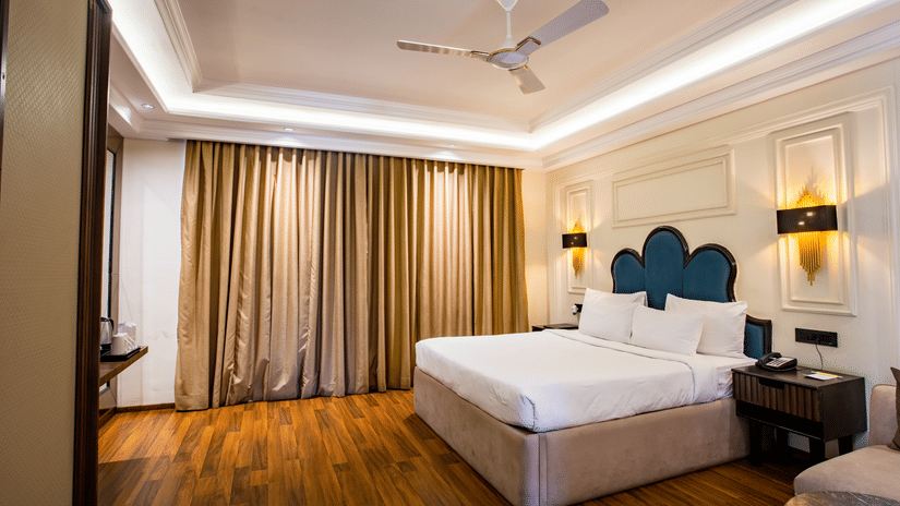 A double bed with side table and a sofa on the side inside one of the rooms of Wedlock Greens Hotel Resorts Dhanbad