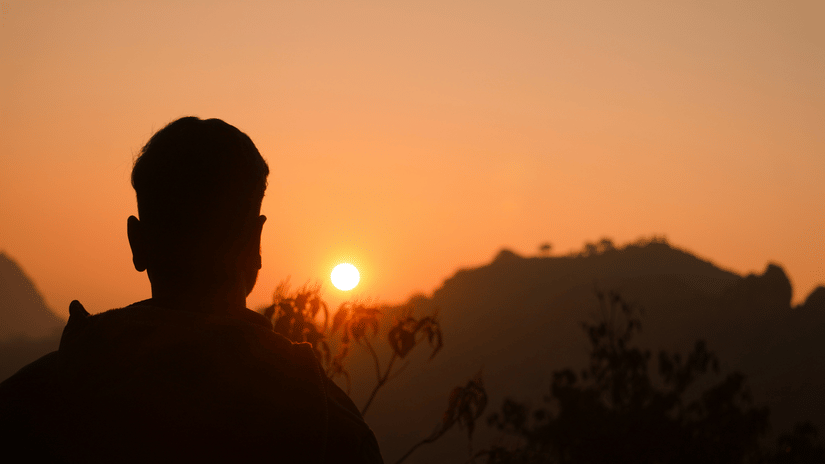 Silhouette of a traveller watching the sunrise over the mountains at Parasnath Hill with golden morning light across the horizon.