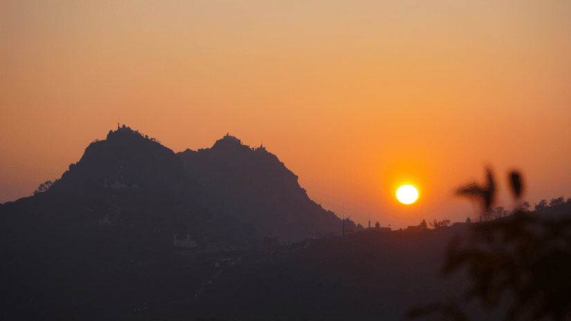 Sun setting behind the mountain ridges of Parasnath Hill, creating a vibrant orange sky and dramatic silhouettes.
