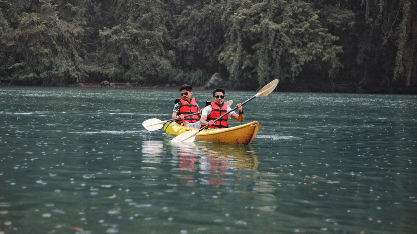 Two people boating in a yellow canoe over a water body with green forest in the background.