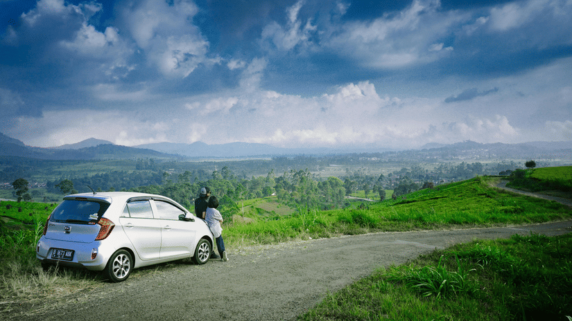 A car parked on a scenic hillside road with lush greenery and mountains of Parasnath, Dhanbad.