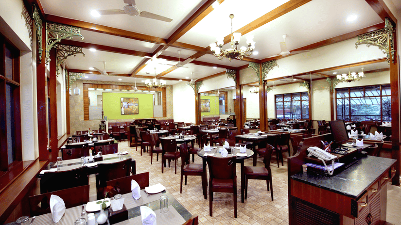 Spacious restaurant at Zara's Resort, Khandala, featuring a well-lit dining hall with neatly set tables and a chandelier, creating a warm, and inviting space for meals.