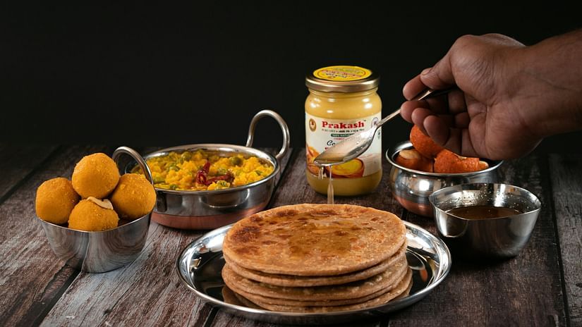 A person pouring ghee on a stack of parathas. 