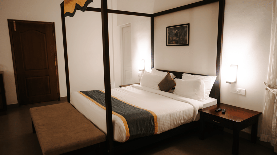 A view of a bedroom shows the four-poster bed and a side table.- Abad Brookside Lakkidi, Wayanad