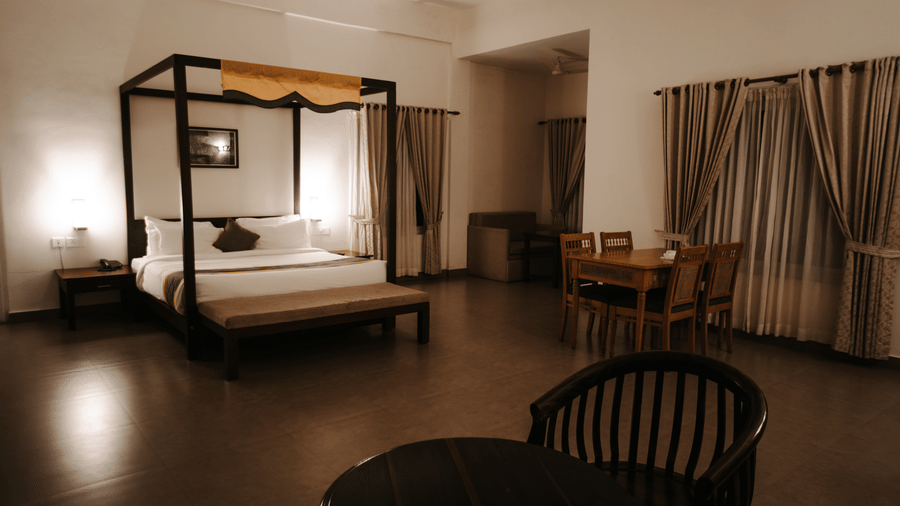 A bedroom features a four-poster bed and a chair, creating a cosy space. - Abad Brookside Lakkidi, Wayanad