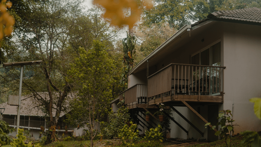 A building with a balcony is surrounded by trees. - Abad Brookside Lakkidi, Wayanad