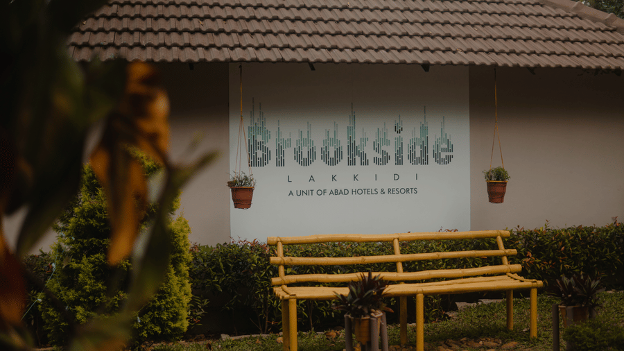 A building features a sign saying 'Brookside'  and a bench.- Abad Brookside Lakkidi, Wayanad