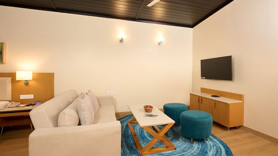 the living room with sofas, a coffee table, ottomans and a tv in the Cottage at ABN Sarovar Portico, Jim Corbett