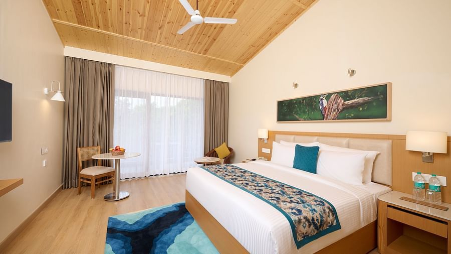 view of a double bed, fan, side table, rug, seating area and other amenities in the Premium room at ABN Sarovar Portico, Jim Corbett
