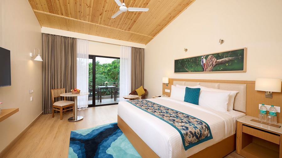 view of a double bed, fan, side table, rug, seating area and other amenities in the Premium room at ABN Sarovar Portico, Jim Corbett