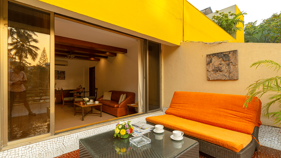 An image of a balcony attached to a room, showcasing an orange sofa and a small coffee table.