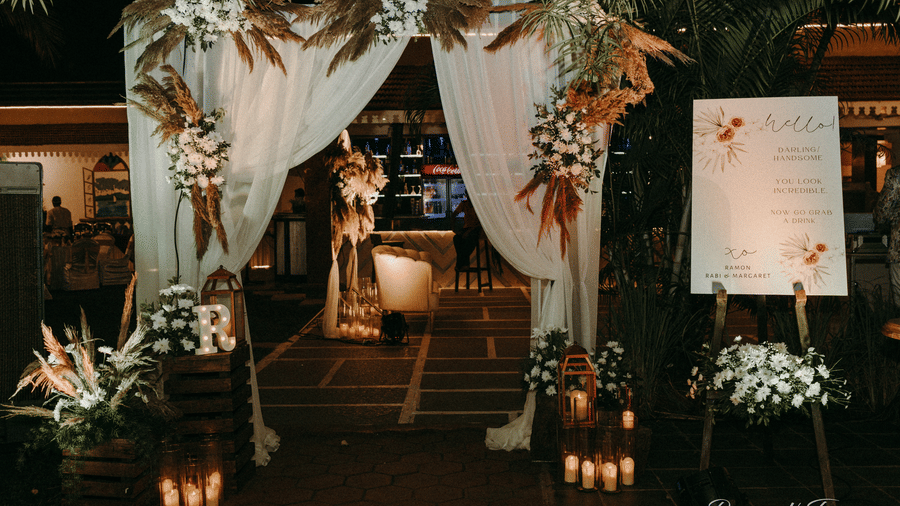 An entry way of an event space decorated with with flowers, candles, placards and white drapery.