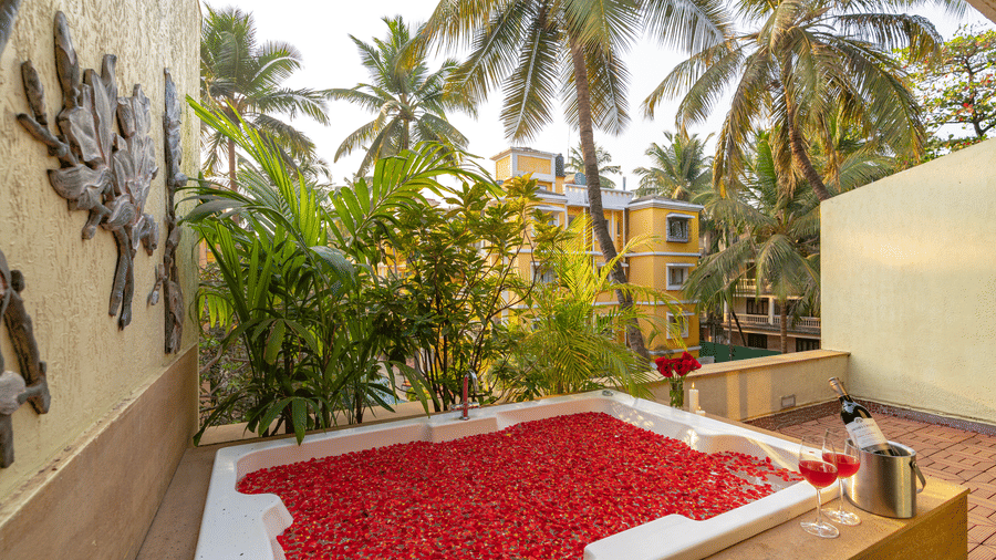 An image of an outdoor bathtub filled with rose petals and water, overlooking palm trees.