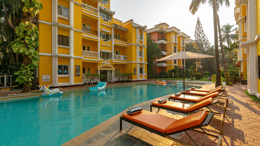 An image of a swimming pool in front of a building, with poolside lounges to rest