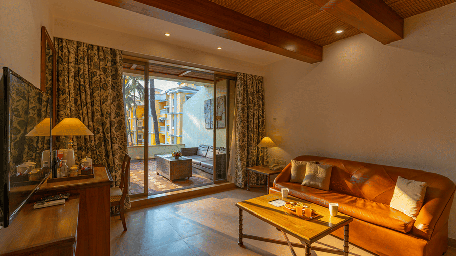 A living room that includes a sofa, coffee table, tea and coffee maker, a TV, and an outdoor balcony with seating arrangements.