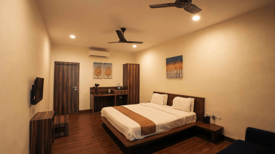 Interior view of a bedroom at Adamo The Village with a double bed, work desk, wall-mounted television, and wooden flooring.