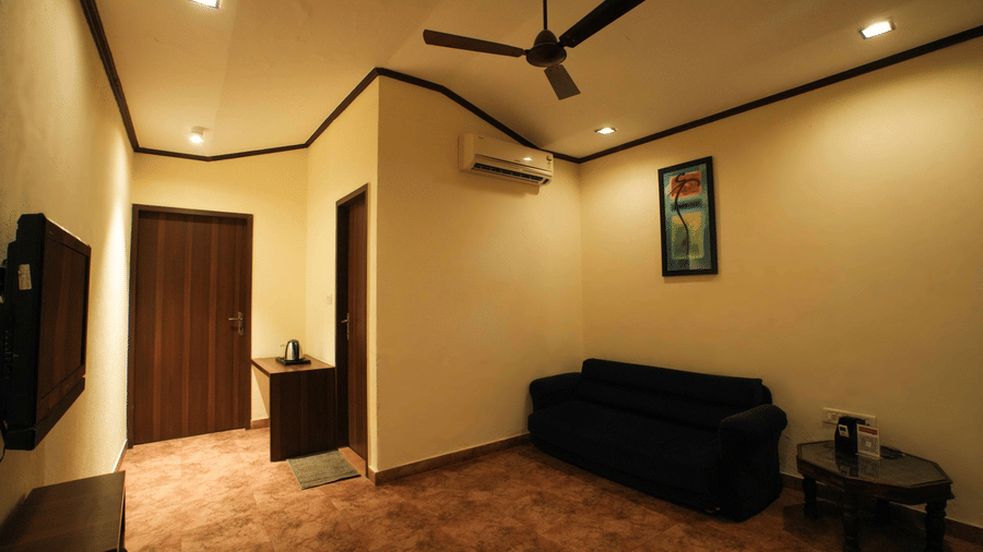 A view of a living area at an accommodation of Adamo The Village with a multi-seating sofa, a wall-mounted TV, and a ceiling fan.