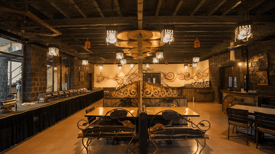 An elegant dining area at Adamo The Village with rustic interiors, wooden ceiling, and neatly arranged tables and chairs.