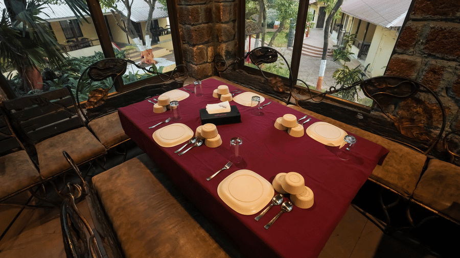 A restaurant table at Adamo The Village set with plates and cups beside large windows overlooking lush greenery.