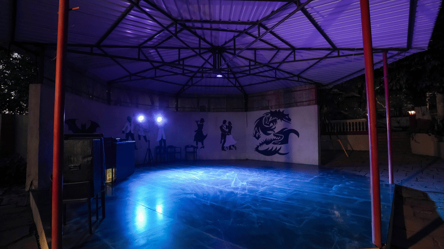 Night view of a covered, open-sided activity space with a metal roof and illuminated floor at Adamo The Village.