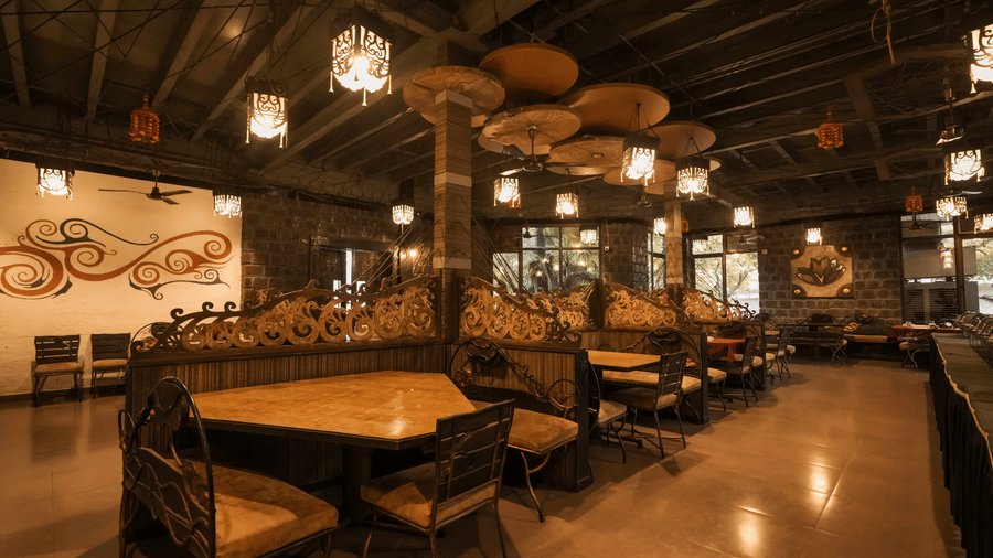 Interior view of a dark, ambient dining hall featuring high-backed booths and elaborate ceiling decorations at Adamo The Village.