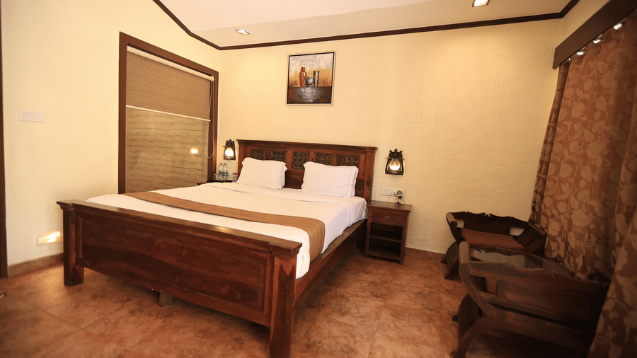A warm hotel bedroom featuring a dark wood double bed frame, bedside tables, and a tile floor.