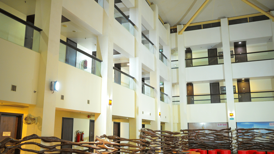 The multi storey atrium at Ambar Sarovar Portico, Gandhidham featuring indoor corridors, glass balconies, a shop, and a seating area with sofas on the ground floor.