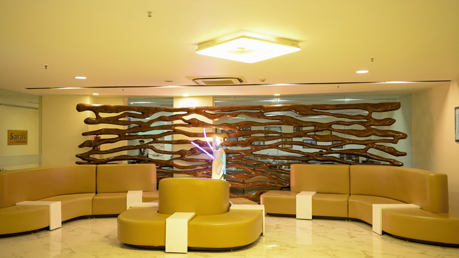 A spacious lobby area at Ambar Sarovar Portico, Gandhidham features curved sofas, a tiled floor, and a large decorative wooden screen against the wall.