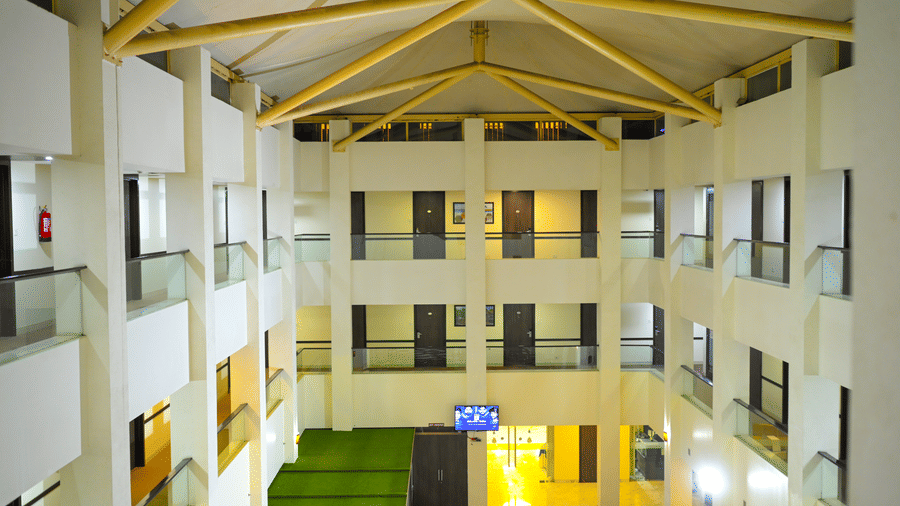 A high angle look inside a multi storey building courtyard at Ambar Sarovar Portico, Gandhidham features white walls, glass balconies, and a ceiling.