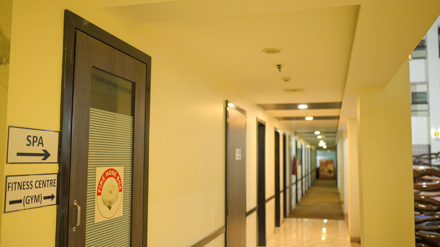 A hotel corridor at Ambar Sarovar Portico, Gandhidham displays directional signboards for the spa, fitness centre, and gym along a well lit hallway.