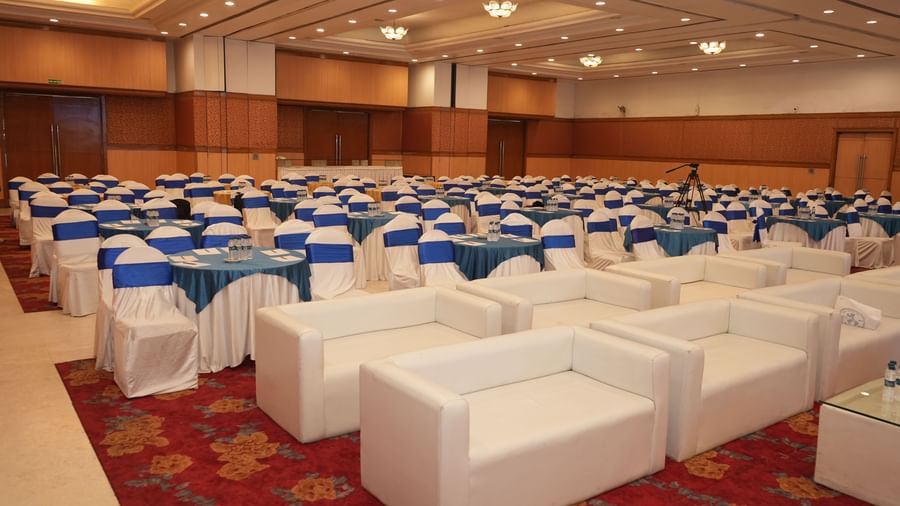  An indoor view of a large conference or banquet hall at Amer Greens, set up with many tables, chairs, and white sofas.