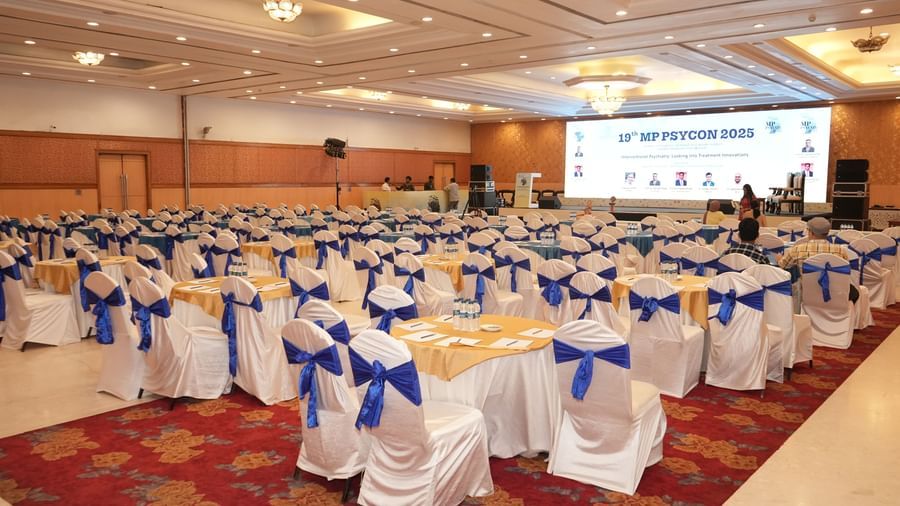  A spacious conference room at Amer Greens is set for a presentation with numerous round tables and chairs, facing a large illuminated projection screen.