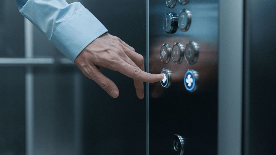 Guest's hand pressing an illuminated call button inside a modern hotel elevator.