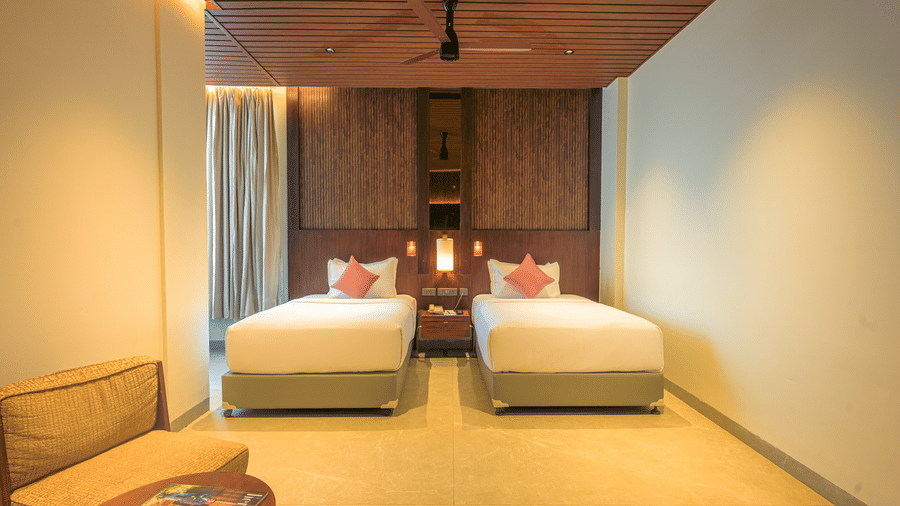 Twin bedroom with two neatly made beds, red accent cushions, wooden ceiling, bedside furnishings and a patterned rug.