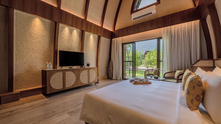 An image of a bedroom with double size bed, flat TV screen with table counter top, and a large window on one side of the room