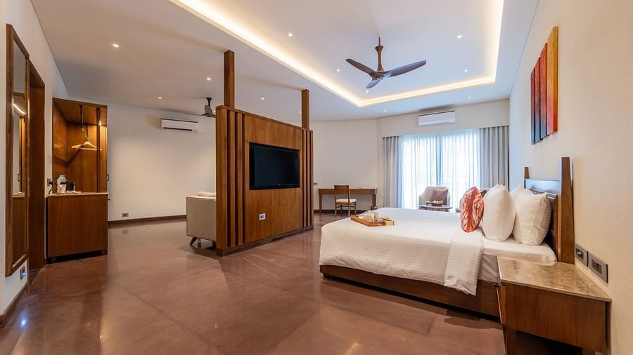 An image of a bedroom with partition, on one side there is a bed and on the other there is a seating area with sofa and table