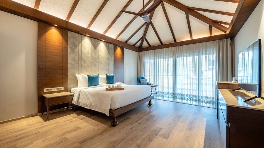 A image of a bedroom with a king size bed, a tea tray placed on it, a flat TV screen with counter top table, and a large window on one side  of the room