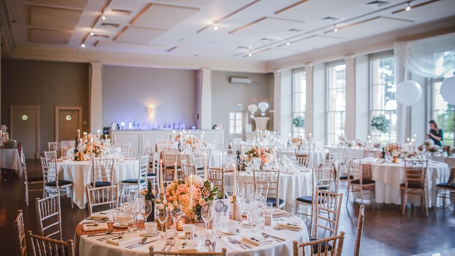 An elaborate banquet hall with round table seating and sun shining through the floor to ceiling windows