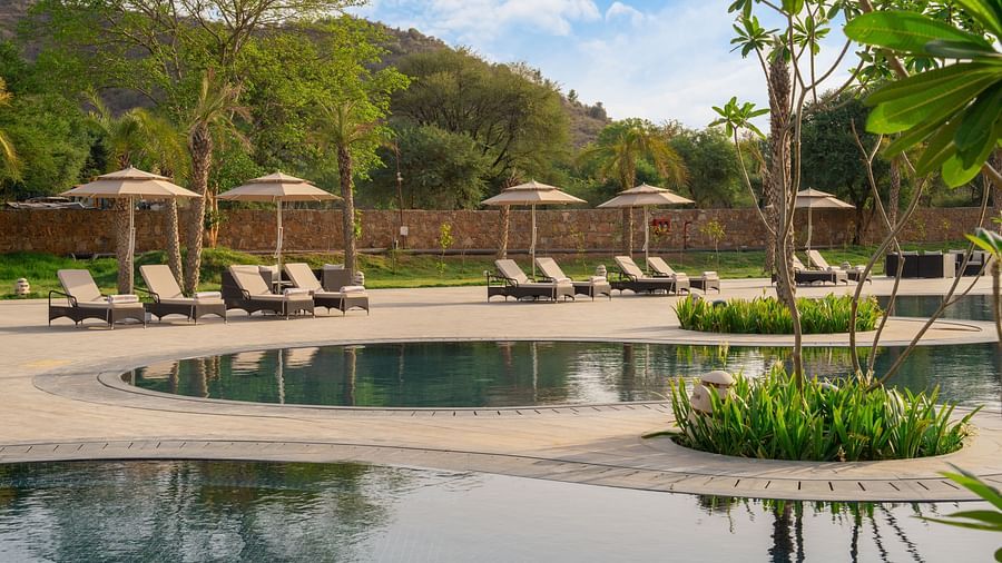 Swimming pool at Ananta Spa and Resort, Ajabgarh with sun-lounger and tress surrounding it.