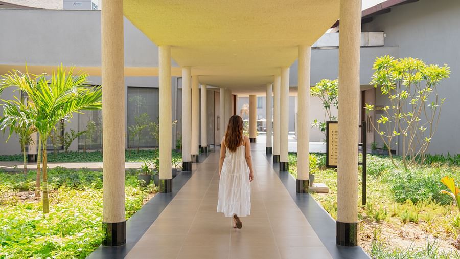 A woman walking through a covered walkway lined with plants and pillars at Ananta Spa and Resort, Ajabgarh.